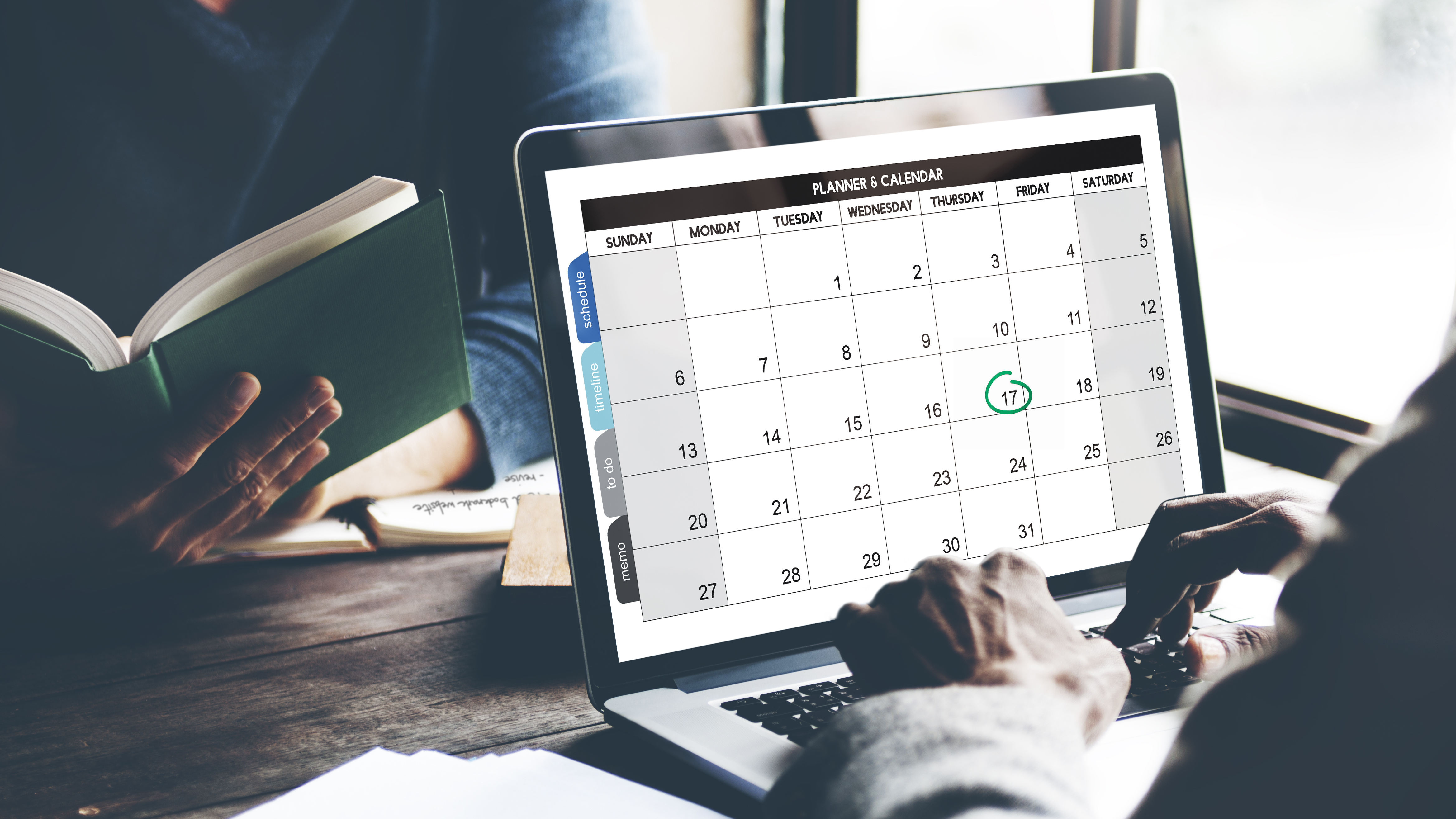 A focused man efficiently working on his laptop while consulting his planner and calendar for a well-organized workflow