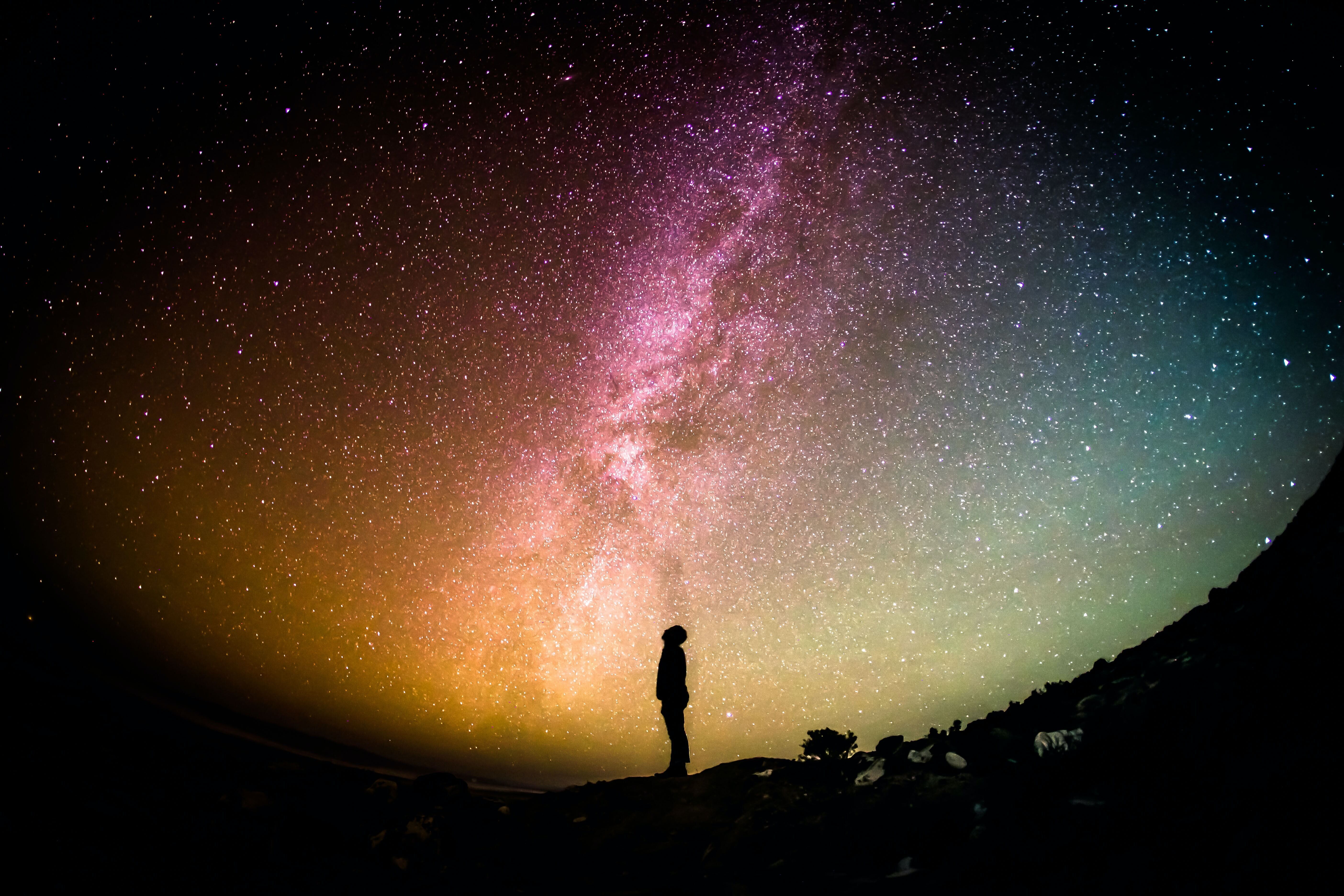 A mesmerizing scene as a man looks up at the vibrant night sky, adorned with the ethereal beauty of the Milky Way, evoking a sense of wonder and cosmic contemplation.