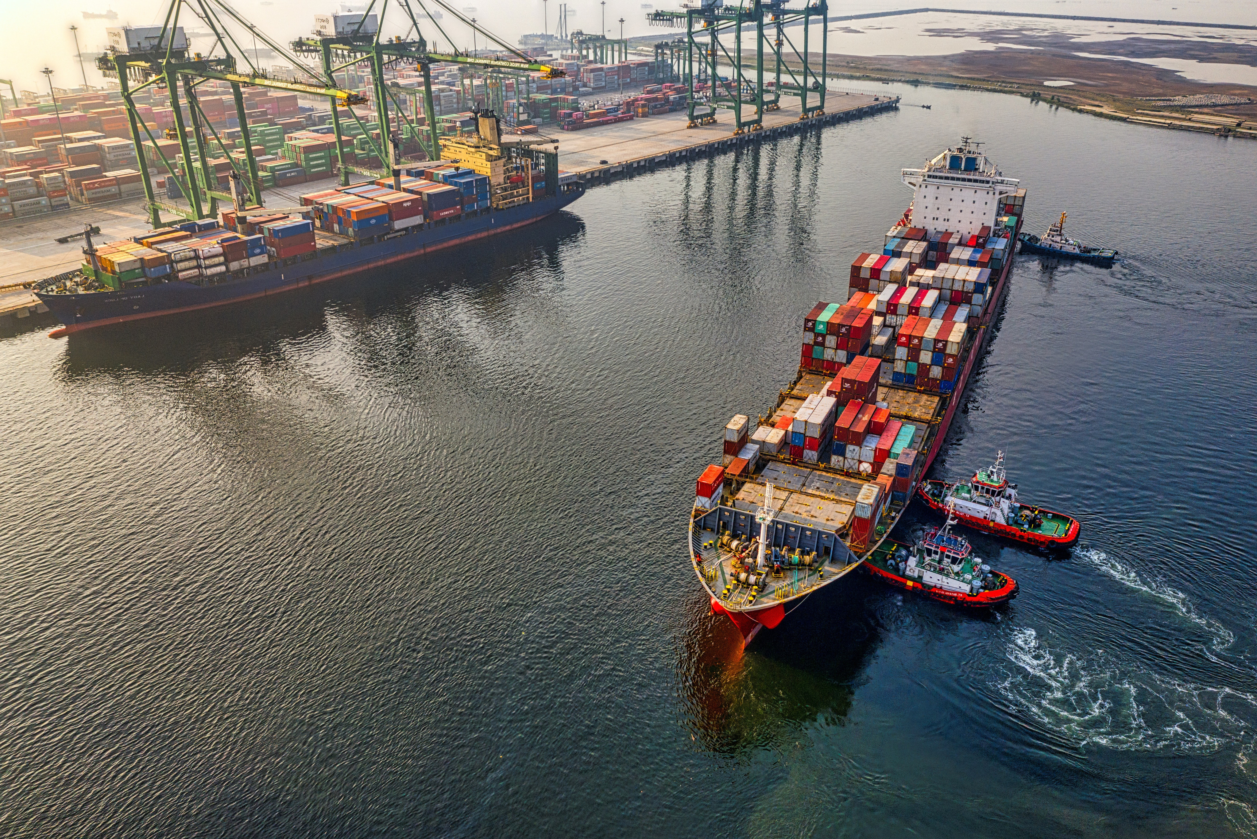 Busy seaport scene as a container ship maneuvers into position for docking, symbolizing the dynamic activities of maritime trade and transportation.