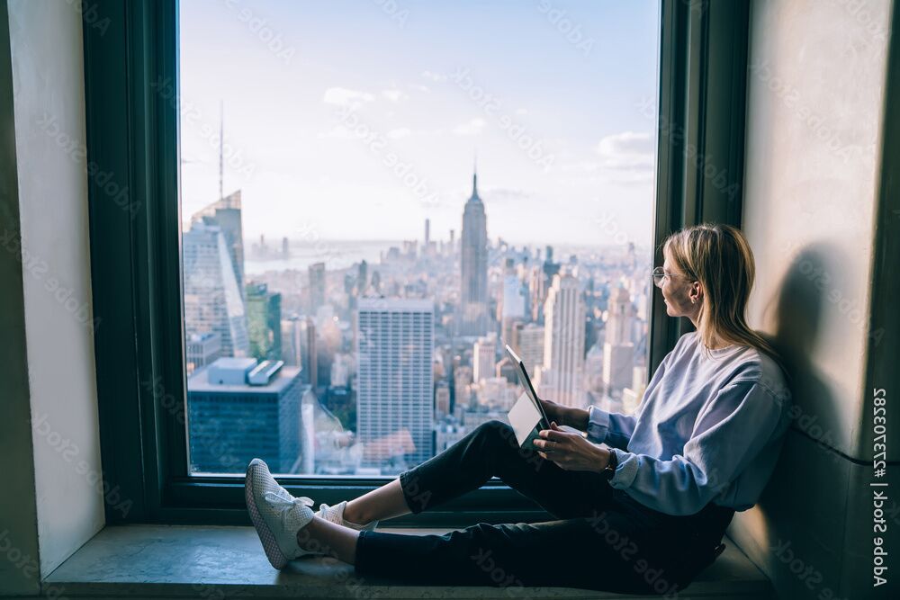 A woman is sitting by a large window overlooking Manhattan. She holds a tablet in her hands and smiles, happy about the work Palas&reg; is doing in the Aerosol Technology sector to provide the present and future generations with a clean and healthy environmen