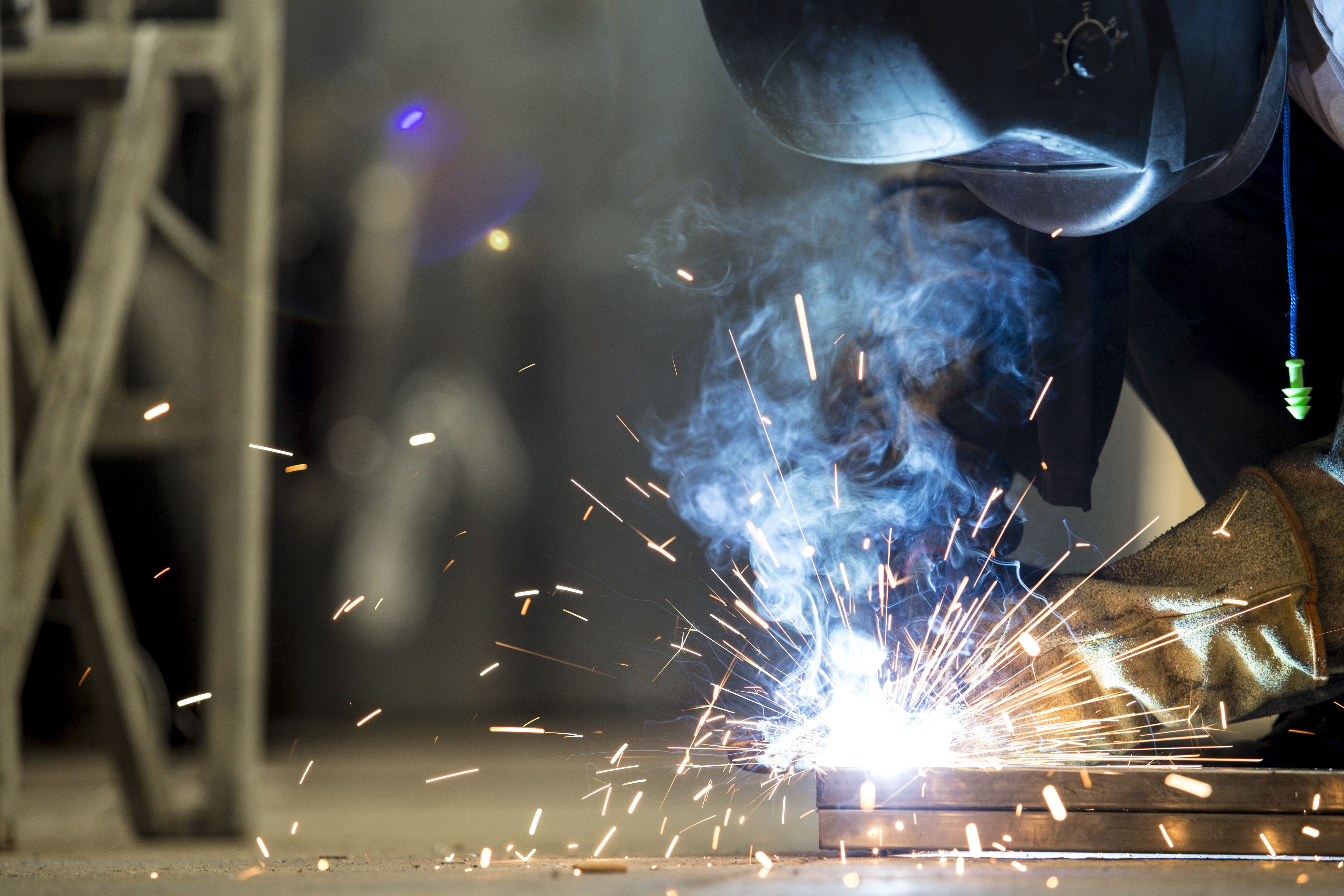 Dynamic image capturing a skilled worker welding metal, sparks flying in all directions. The craftsman is clad in protective clothing for safety during the welding process.