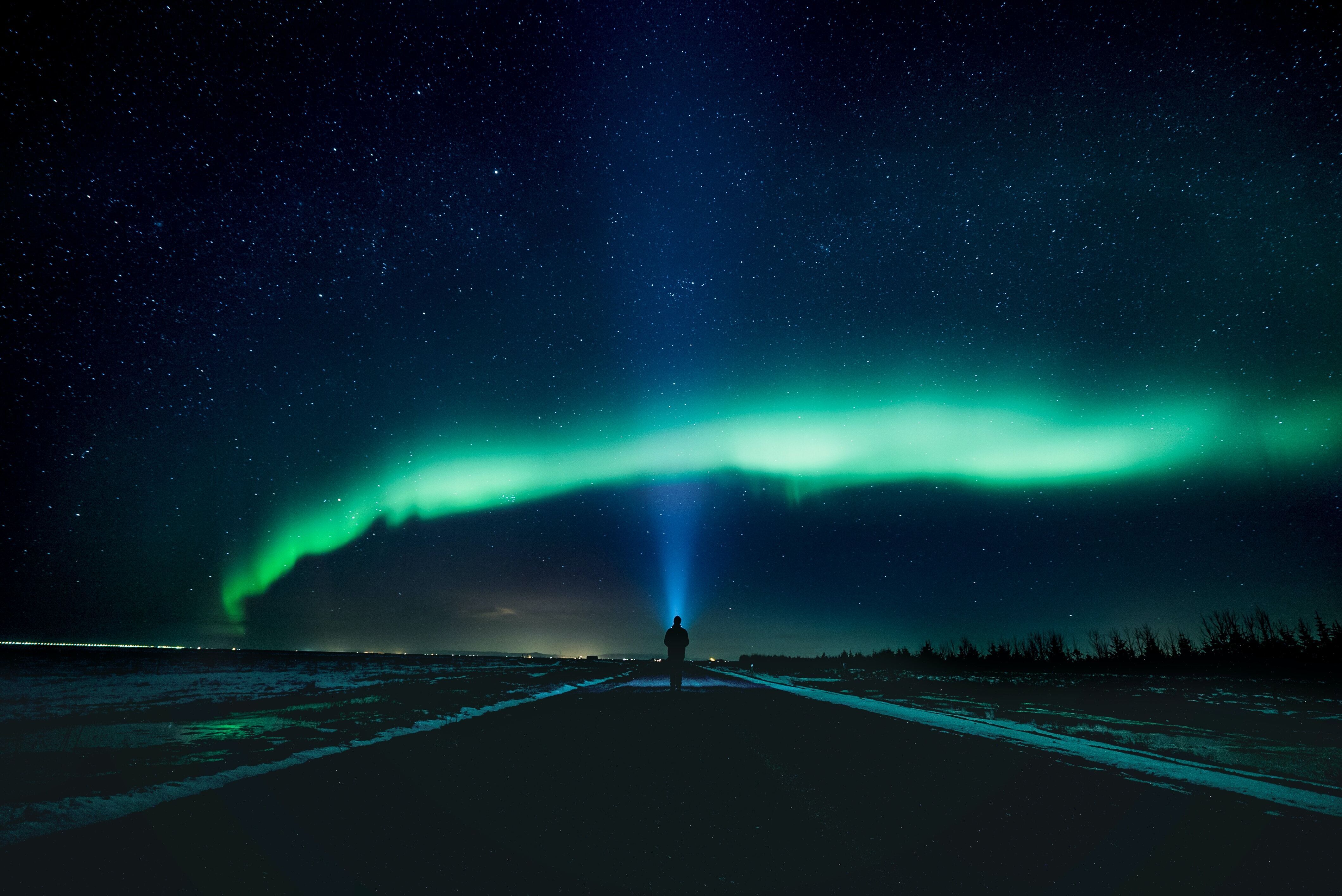 A captivating scene of a man walking on an icy street, looking up at the stars, with polar lights gracefully crossing the night sky above.