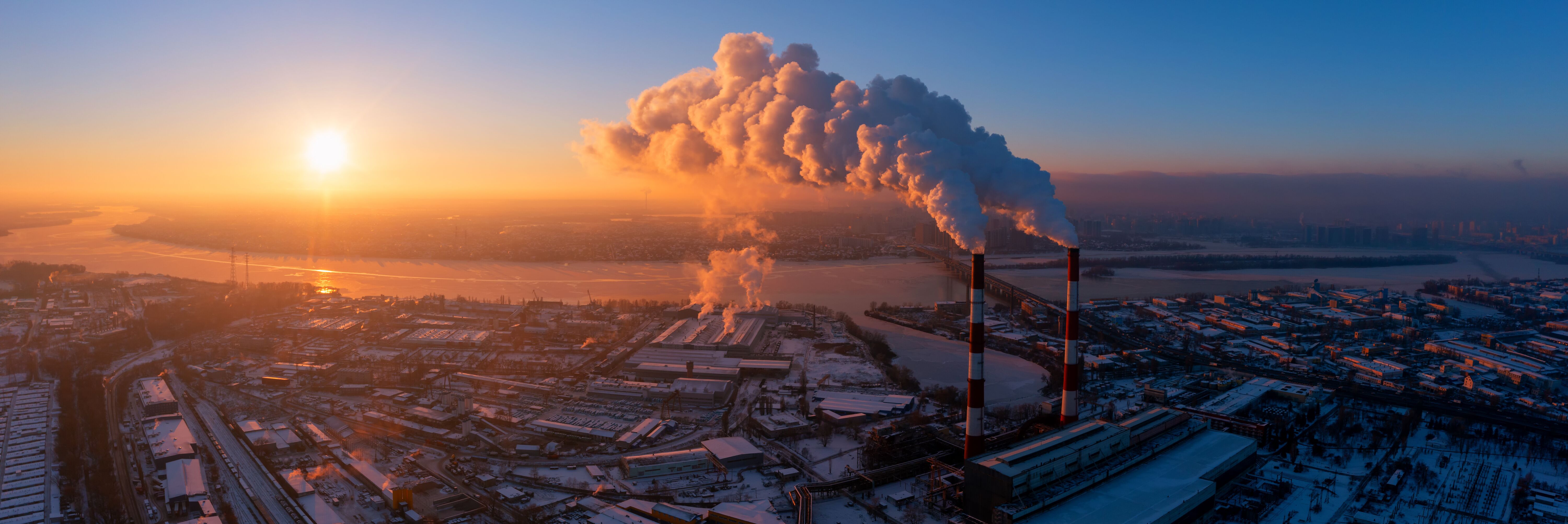 The harbour of a city and industrial buildings during sunset, one of the factories' chimney evaporates a large cloud. Palas® provides solutions and devices to monitor outdoor air quality and detect pollutants.