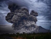 Intense image of a volcano with huge dark ash clouds billowing into the sky, depicting environmental challenges related to fine dust and pollution.